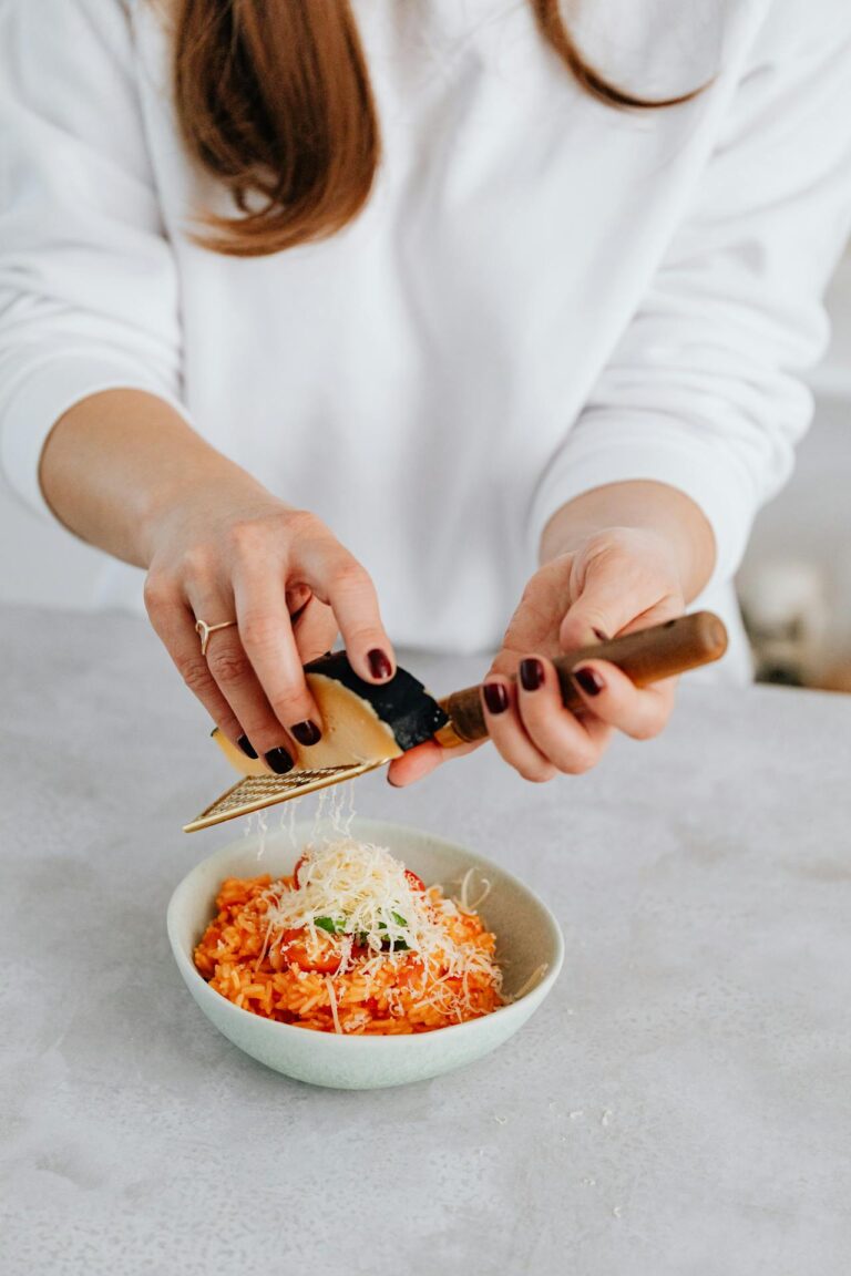 woman grating a block of cheese into a bowl of food